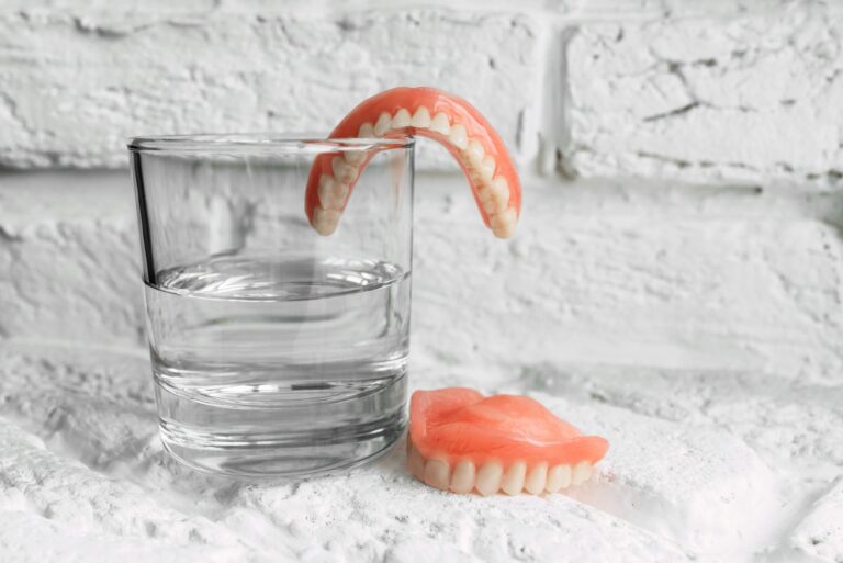 A denture in a glass of water. Dental prosthesis care. Full removable plastic denture of the jaws