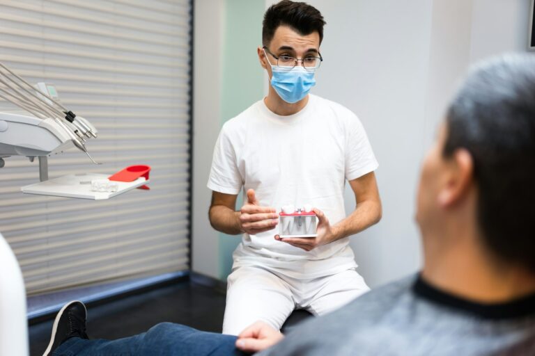 Dental surgeon with dental crown in hands model talks to patient about prosthetics.